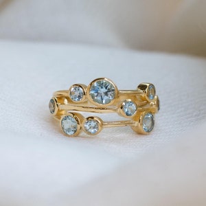 Puede incluir: Un anillo de oro con múltiples pequeñas piedras preciosas azules engastadas en una banda delicada.
