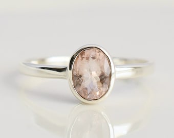 May include: A silver ring with a light pink oval gemstone.