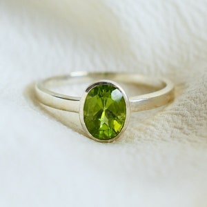 May include: A silver ring with a green oval gemstone. The ring is on a white fabric background.