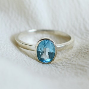May include: A silver ring with a light blue oval gemstone.