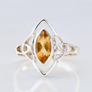 May include: A silver ring with a Celtic knot design and a marquise-shaped topaz gemstone.
