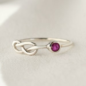 May include: A silver ring with a knot design and a single ruby gemstone.