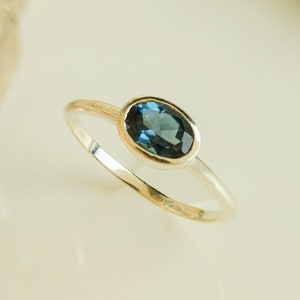 Könnte beinhalten: Ein silberner Ring mit einem blauen ovalen Edelstein.