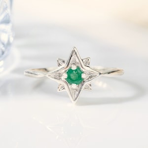 Op de afbeelding: Een zilveren ring met een groene smaragd in een stervormig ontwerp.
