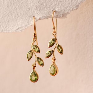 Puede incluir: Pendientes de oro con un delicado diseño de rama adornado con piedras preciosas de peridoto verde. Los pendientes tienen un peridoto en forma de pera que cuelga en la parte inferior.