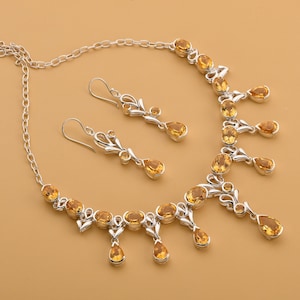 May include: A silver necklace and earrings set with teardrop-shaped topaz gemstones. The necklace has a delicate chain and a pendant with multiple topaz stones. The earrings are dangle style with a single topaz stone.