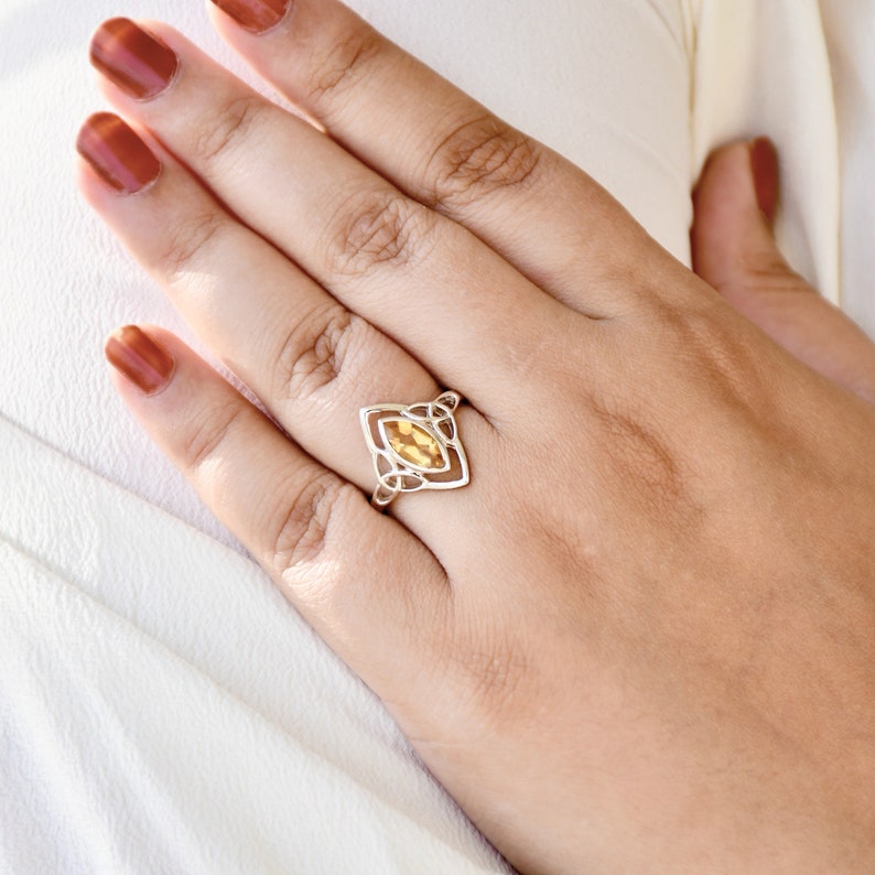 May include: A silver ring with a yellow gemstone set in a Celtic knot design.