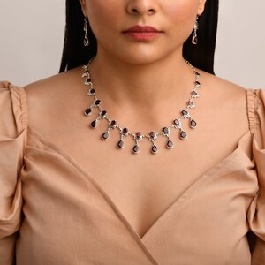 Puede incluir: Un collar de plata con un colgante de granate en forma de l&aacute;grima. El collar tiene una cadena delicada y est&aacute; adornado con peque&ntilde;as piedras brillantes.