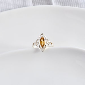 May include: A silver ring with a Celtic knot design and a marquise-shaped topaz gemstone.