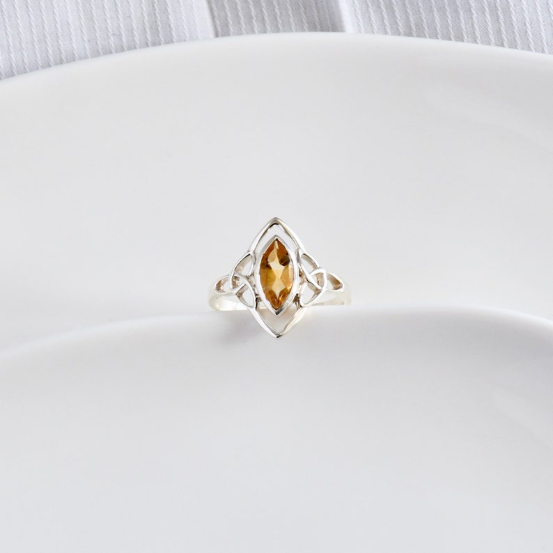 May include: A silver ring with a Celtic knot design and a marquise-shaped topaz gemstone.