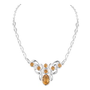 Op de afbeelding: Een zilveren ketting met een decoratief ontwerp. Het heeft ovale en ronde oranje-gele edelstenen. De ketting heeft een ketting met ovale schakels. De edelstenen zijn gezet in een gestileerd bloemmotief.