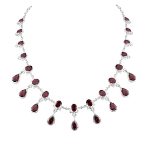 Puede incluir: Un collar de plata con un dise&ntilde;o delicado presenta una fila de gotas de piedras preciosas rojas colgantes. El collar est&aacute; adornado con m&uacute;ltiples piedras preciosas rojas de forma ovalada.