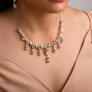 May include: A silver necklace with a delicate chain and a pendant featuring a teardrop-shaped topaz gemstone. The necklace is adorned with smaller topaz gemstones along the chain.