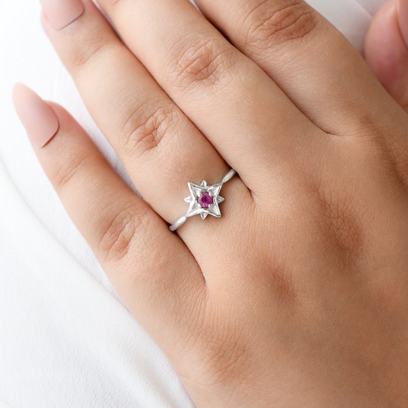 Op de afbeelding: Een zilveren ring met een ontwerp van een vijfpuntige ster met een roze edelsteen in het midden.