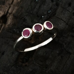 Peut inclure: Une bague en argent avec trois pierres pr&eacute;cieuses rondes rouges dispos&eacute;es en rang&eacute;e.