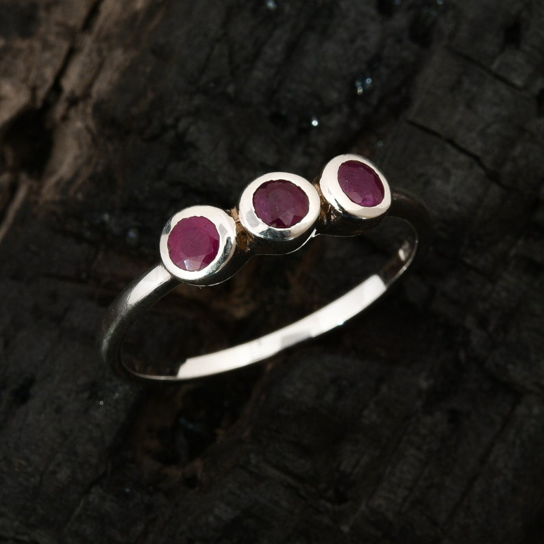 Peut inclure: Une bague en argent avec trois pierres pr&eacute;cieuses rondes rouges dispos&eacute;es en rang&eacute;e.