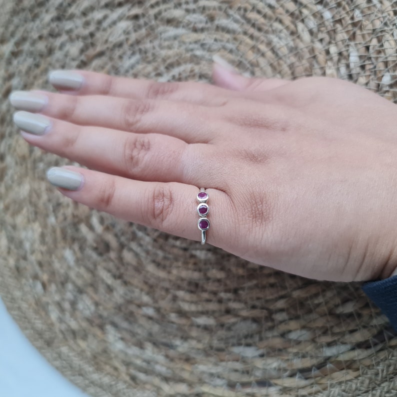 Peut inclure: Une bague en argent avec trois petites pierres pr&eacute;cieuses rondes rouges dispos&eacute;es en rang&eacute;e.
