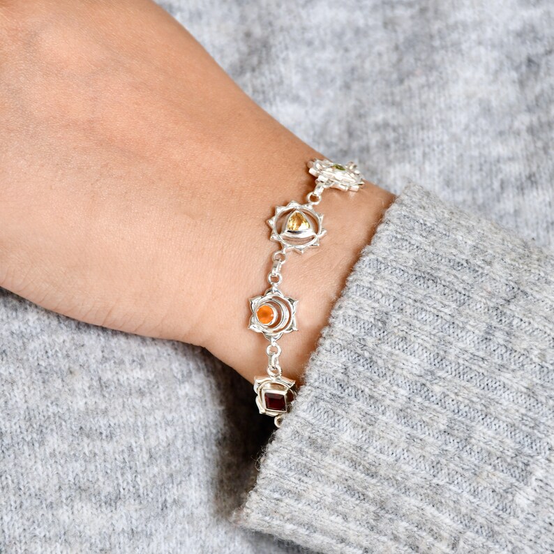 May include: A silver bracelet with seven charms, each featuring a different colored gemstone and a silver mandala design. The gemstones are red, orange, yellow, green, blue, indigo, and violet.
