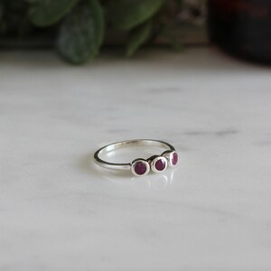 Peut inclure: Une bague en argent avec quatre petites pierres pr&eacute;cieuses rondes rouges dispos&eacute;es en rang&eacute;e.