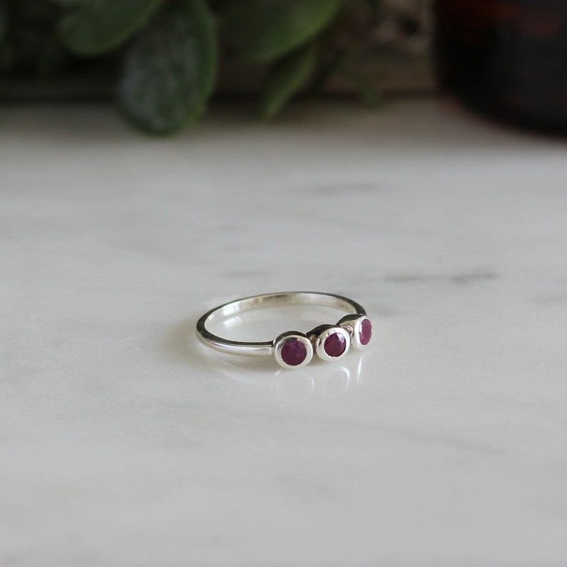 Peut inclure: Une bague en argent avec quatre petites pierres pr&eacute;cieuses rondes rouges dispos&eacute;es en rang&eacute;e.