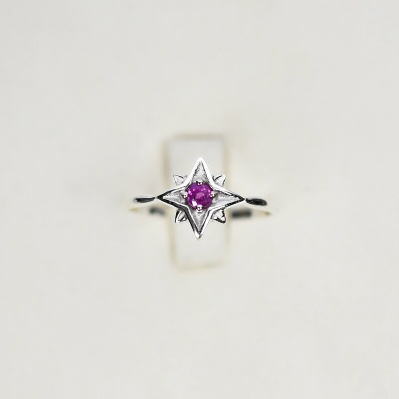 Op de afbeelding: Een zilveren ring met een roze edelsteen in een stervormig ontwerp.
