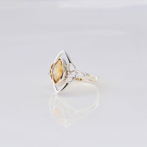 May include: A silver ring with a Celtic knot design and a yellow citrine gemstone.