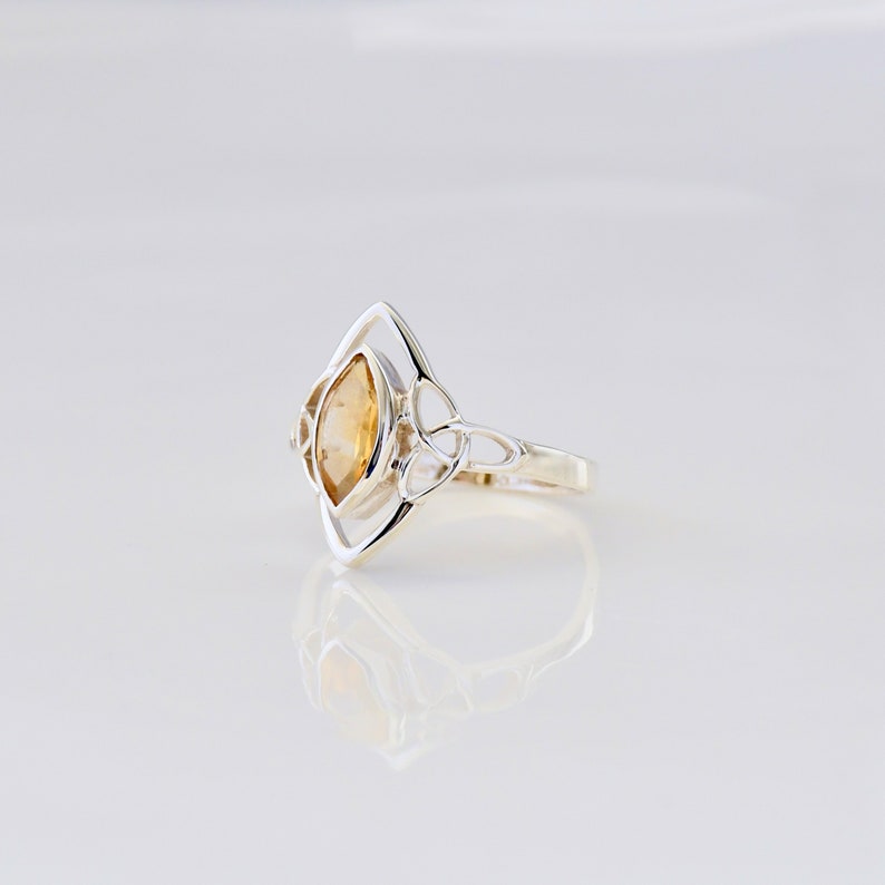 May include: A silver ring with a Celtic knot design and a yellow citrine gemstone.
