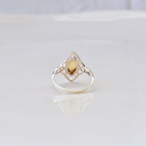May include: A silver ring with a Celtic knot design and a clear, yellow-brown gemstone in the center.