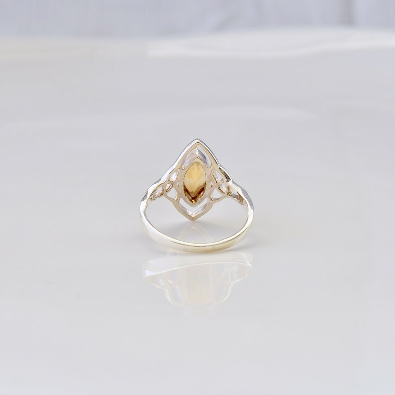 May include: A silver ring with a Celtic knot design and a clear, yellow-brown gemstone in the center.