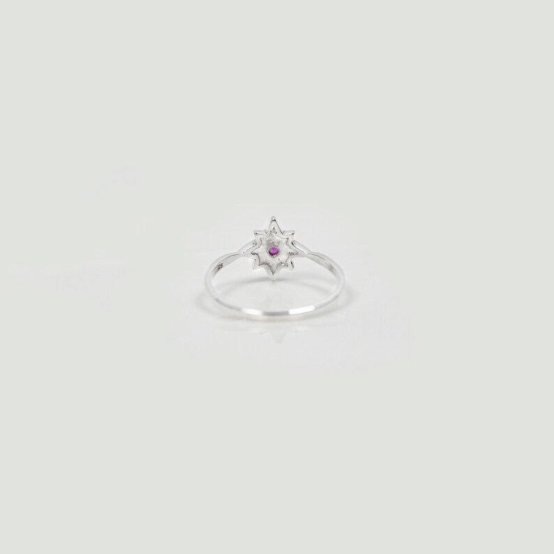 Op de afbeelding: Een zilveren ring met een stervormig ontwerp met een klein roze edelsteentje in het midden.