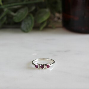 Peut inclure: Une bague en argent avec trois petites pierres rondes rouges.