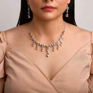 May include: A silver necklace with a delicate design featuring teardrop-shaped yellow gemstones. The necklace has a matching pair of earrings with the same design.