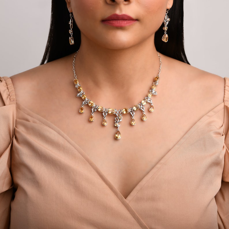 May include: A silver necklace with a delicate design featuring teardrop-shaped yellow gemstones. The necklace has a matching pair of earrings with the same design.