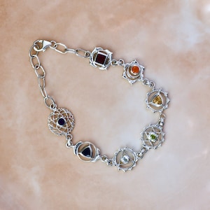 May include: Silver bracelet with seven chakra symbols, each with a different colored gemstone. The gemstones are red, orange, yellow, green, blue, indigo, and violet.