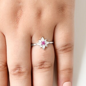 Op de afbeelding: Een zilveren ring met een roze edelsteen in het midden, in de vorm van een ster.