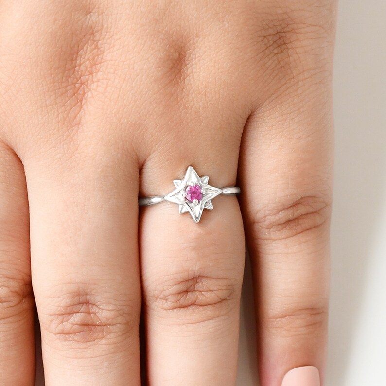 Op de afbeelding: Een zilveren ring met een roze edelsteen in het midden, in de vorm van een ster.