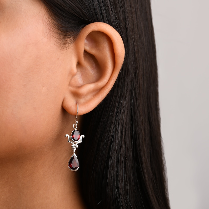 Puede incluir: Pendientes de plata con dos gotas de piedras preciosas rojas. Los pendientes tienen un dise&ntilde;o delicado y adornado.