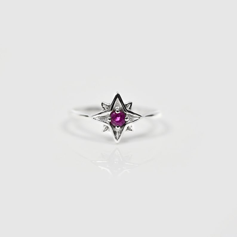 Op de afbeelding: Een zilveren ring met een roze edelsteen in het midden, omringd door een stervormig ontwerp.