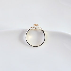 May include: A silver ring with a single, round, light brown gemstone set in the center. The ring is simple and elegant.