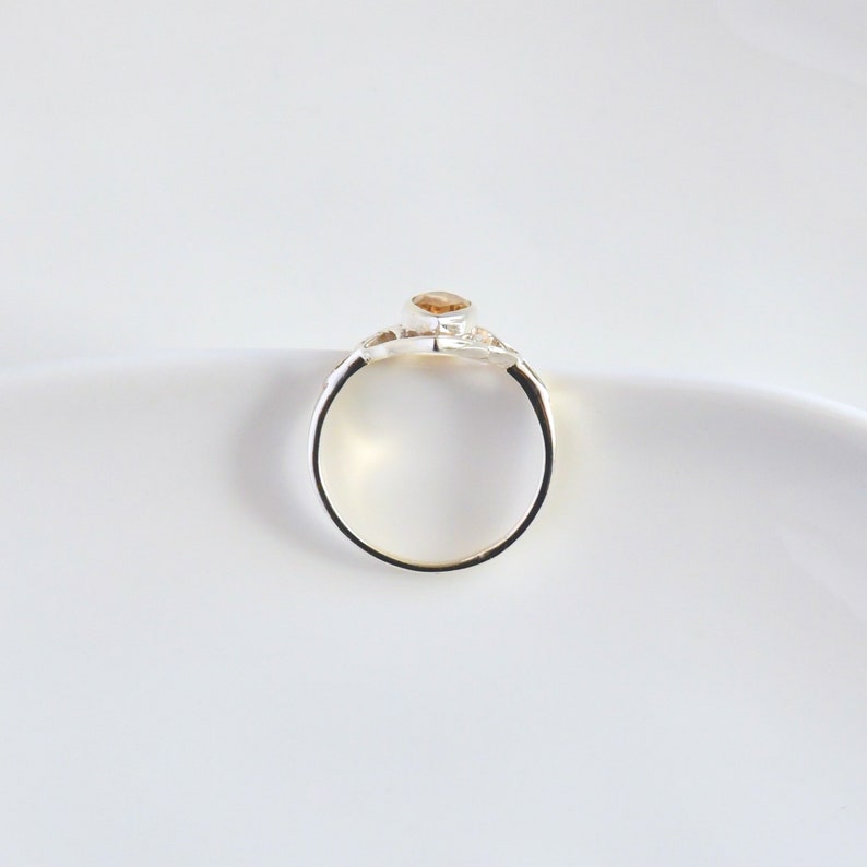 May include: A silver ring with a single, round, light brown gemstone set in the center. The ring is simple and elegant.