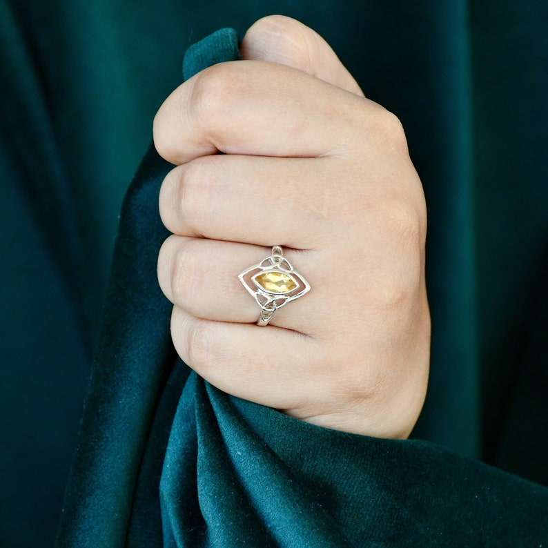 May include: A silver ring with a yellow gemstone set in a Celtic knot design.