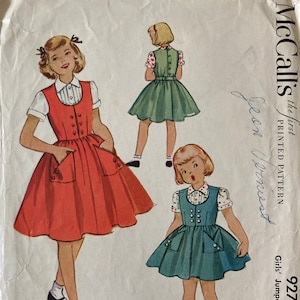 May include: Vintage McCall's sewing pattern for a girl's jumper and blouse. The illustration shows three girls wearing jumpers in red, green, and teal, paired with blouses. The pattern number is 9271, size 4.