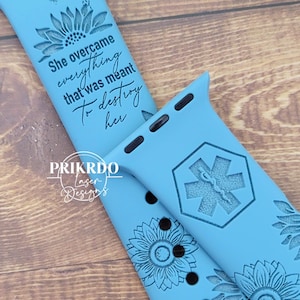 May include: Two blue silicone watch bands with engraved designs. One band features a sunflower and the text "She overcame everything that was meant to destroy her". The other band features a sunflower and a medical symbol.