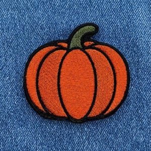 May include: An embroidered patch shaped like a pumpkin with bright orange segments, a dark green stem, and a thick black border. The pumpkin features detailed vertical stitching lines that define its rounded shape and texture against a blue fabric.