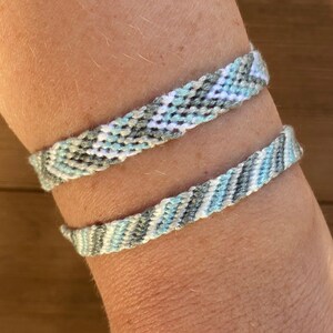 May include: Two friendship bracelets in a blue, white and grey chevron pattern.