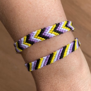 May include: Two friendship bracelets with a chevron pattern in purple, yellow and black colours.