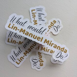 Puede incluir: Un conjunto de pegatinas blancas con letras doradas que dicen "What would Lin-Manuel Miranda Do?" Las pegatinas est&aacute;n apiladas sobre una superficie blanca.