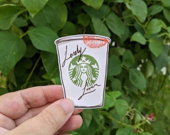 Könnte beinhalten: Ein weißer Kaffebecher mit einem grünen Starbucks-Logo und den Worten "lonely lover" darauf. Auf dem Becher befindet sich ein roter Lippenstift-Abdruck.