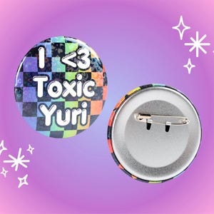 May include: Two round pinback buttons. One button features a colorful checkered pattern with the text "I <3 Toxic Yuri". The other button shows the back with a safety pin. The background is a gradient of pink and purple.