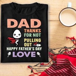 Puede incluir: Camiseta negra con un diseño humorístico para el Día del Padre. El diseño presenta la palabra "DAD" en color melocotón, junto con el texto "THANKS FOR NOT PULLING OUT" y "HAPPY FATHER'S DAY LOVE". El diseño incluye espermatozoides de dibujos animados.